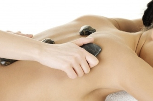 Bodywork therapist applying hot stones on person's back.